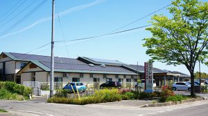 太陽光パネル付きの平屋建て介護施設の外観。駐車場と周辺環境を含む
